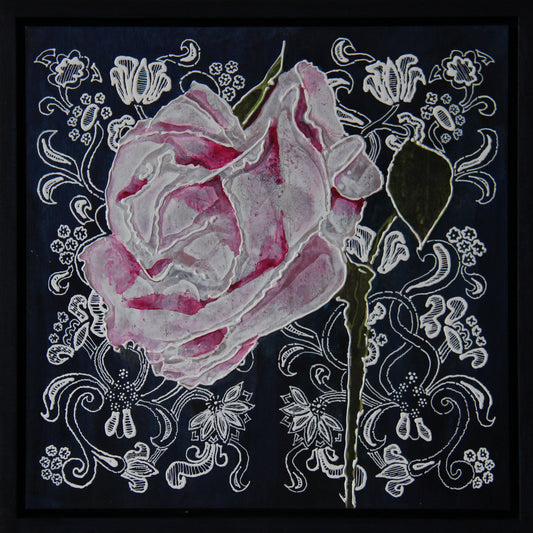 A framed square art piece featuring a large pink rose with white and gray shading, set against a dark navy background with intricate white floral scrollwork. The piece is enclosed in a thin black frame.