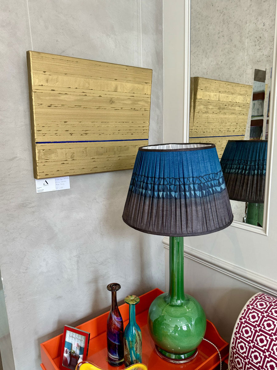 An abstract painting featuring vertical textured oil paint stripes in gold with one prominent delft blue stripe running across the centre in a colourful living room.