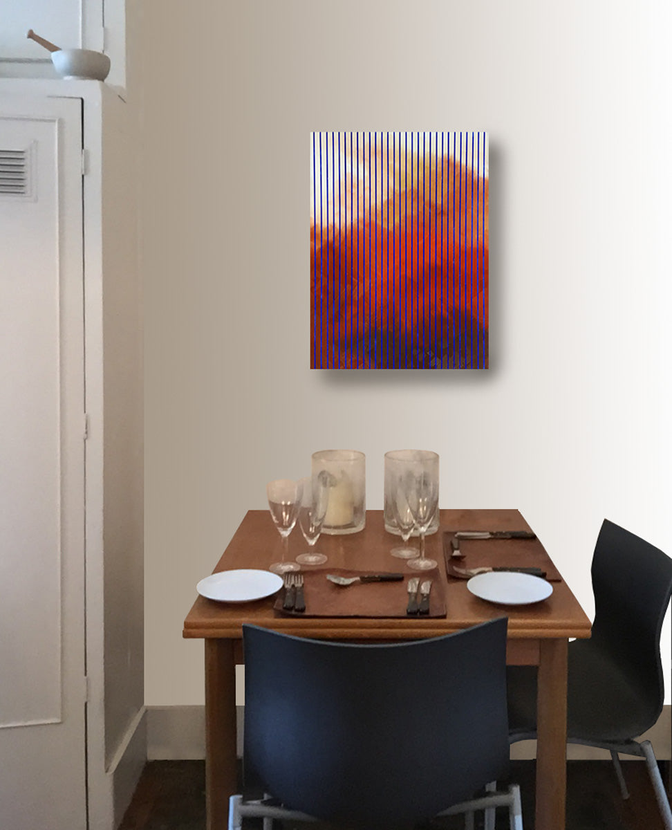 An abstract painting on a deep gesso panel with red, orange, and blue vertical striped cloud patterns, displayed on a beige wall above a wooden dining table set with plates and chairs.