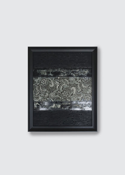A framed abstract art painting featuring textured black sections and a central horizontal band with gray and white paisley lace patterns, displayed against a light gray wall.