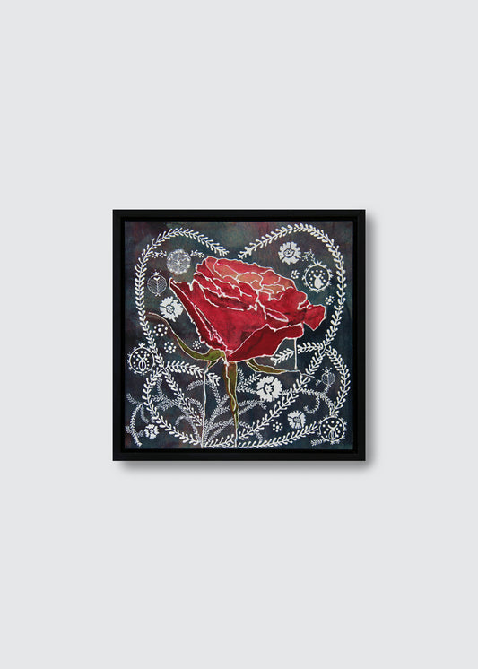 A framed art print featuring a vibrant red rose surrounded by intricate white floral patterns on a dark background, enclosed in a simple black frame against a light gray wall.