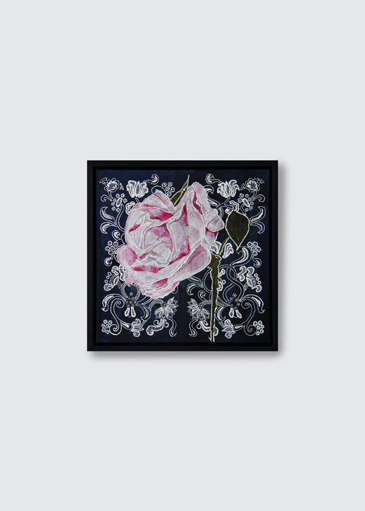 A framed square art painting featuring a pink rose with white ornamental floral details on a dark navy background, shown against a light gray wall.
