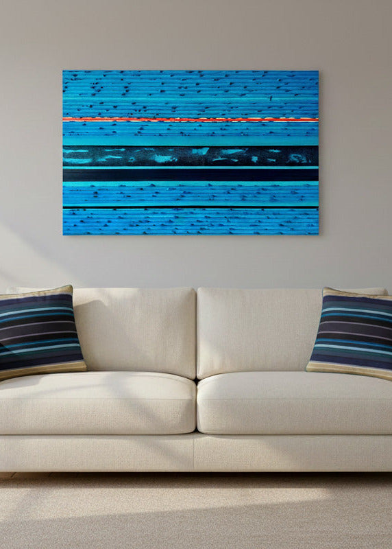 A modern living room setup featuring a cream-colored sofa with two blue and navy striped throw pillows, flanked by matching side tables and lamps, with a turquoise blue abstract canvas painting hanging on the wall above.