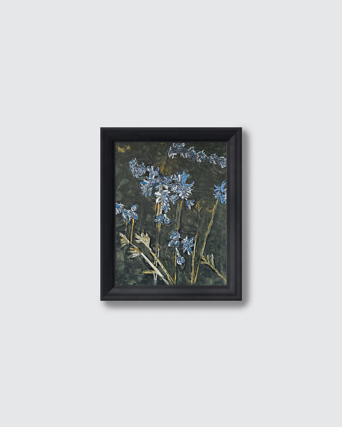 A framed art print featuring bluebells on a dark textured background, enclosed in a simple black frame against a light gray wall.