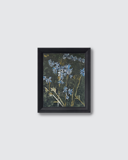 A framed art print featuring bluebells on a dark textured background, enclosed in a simple black frame against a light gray wall.
