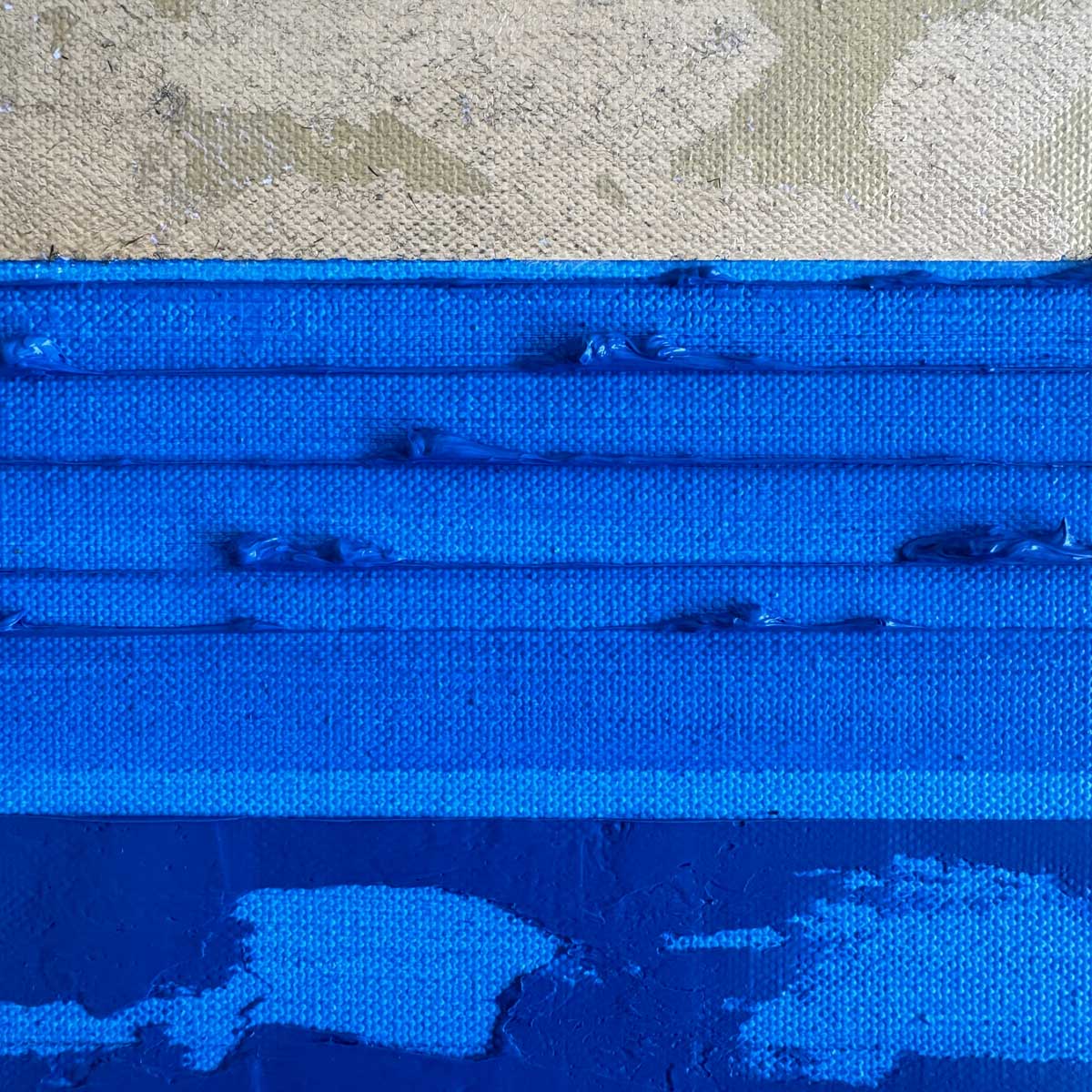 A close-up of a blue textured oil canvas surface with horizontal ridges, a gold leaf section at the top.
