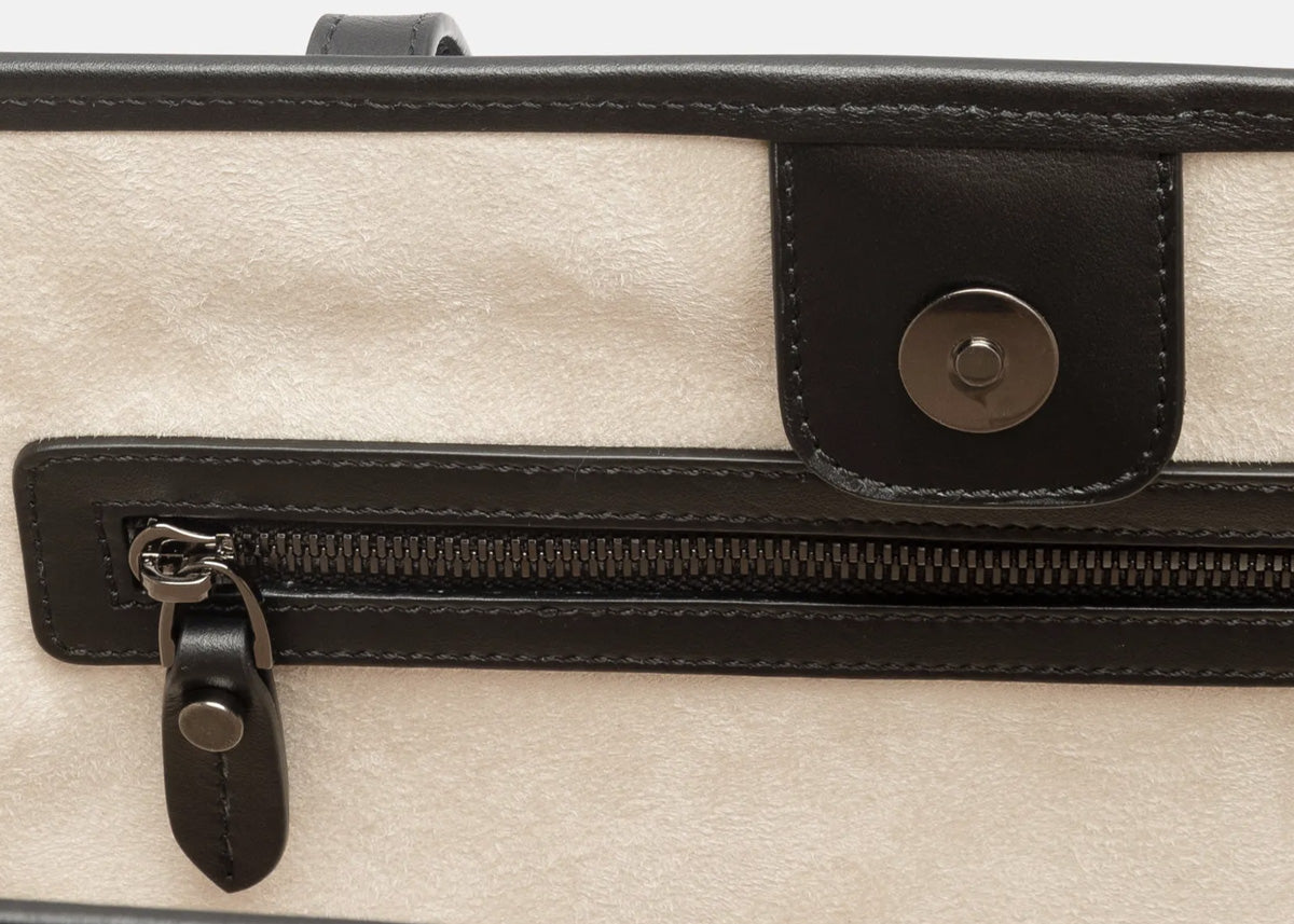 Close-up of a beige textured faux suede interior of tote bag with black leather trim, a horizontal zipper pocket, and a snap-button flap.