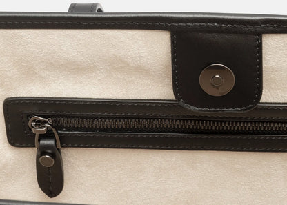 Close-up of a beige textured faux suede interior of tote bag with black leather trim, a horizontal zipper pocket, and a snap-button flap.