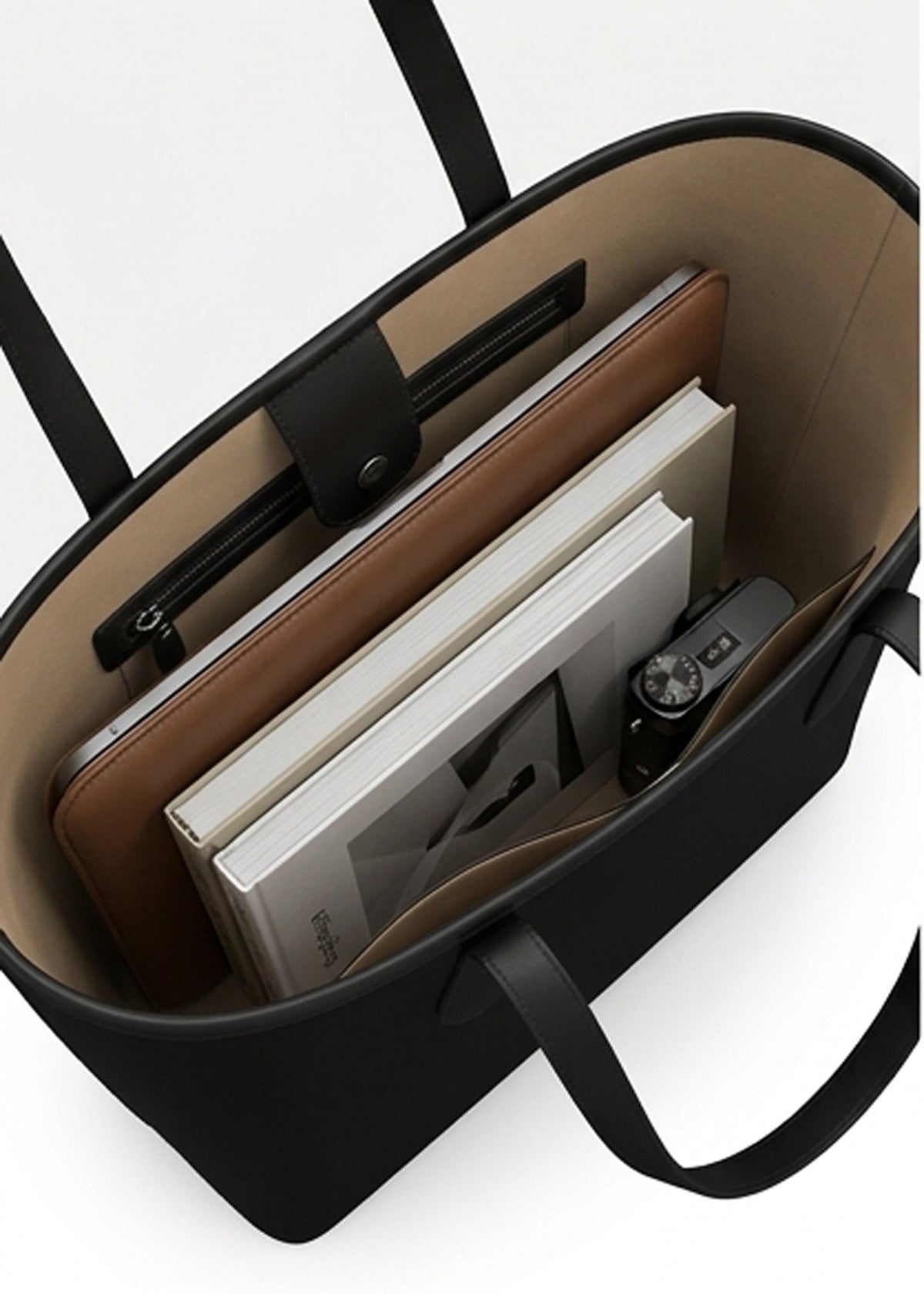 Black tote bag shown from above, filled with books, a brown folio, and a camera, on a white background.
