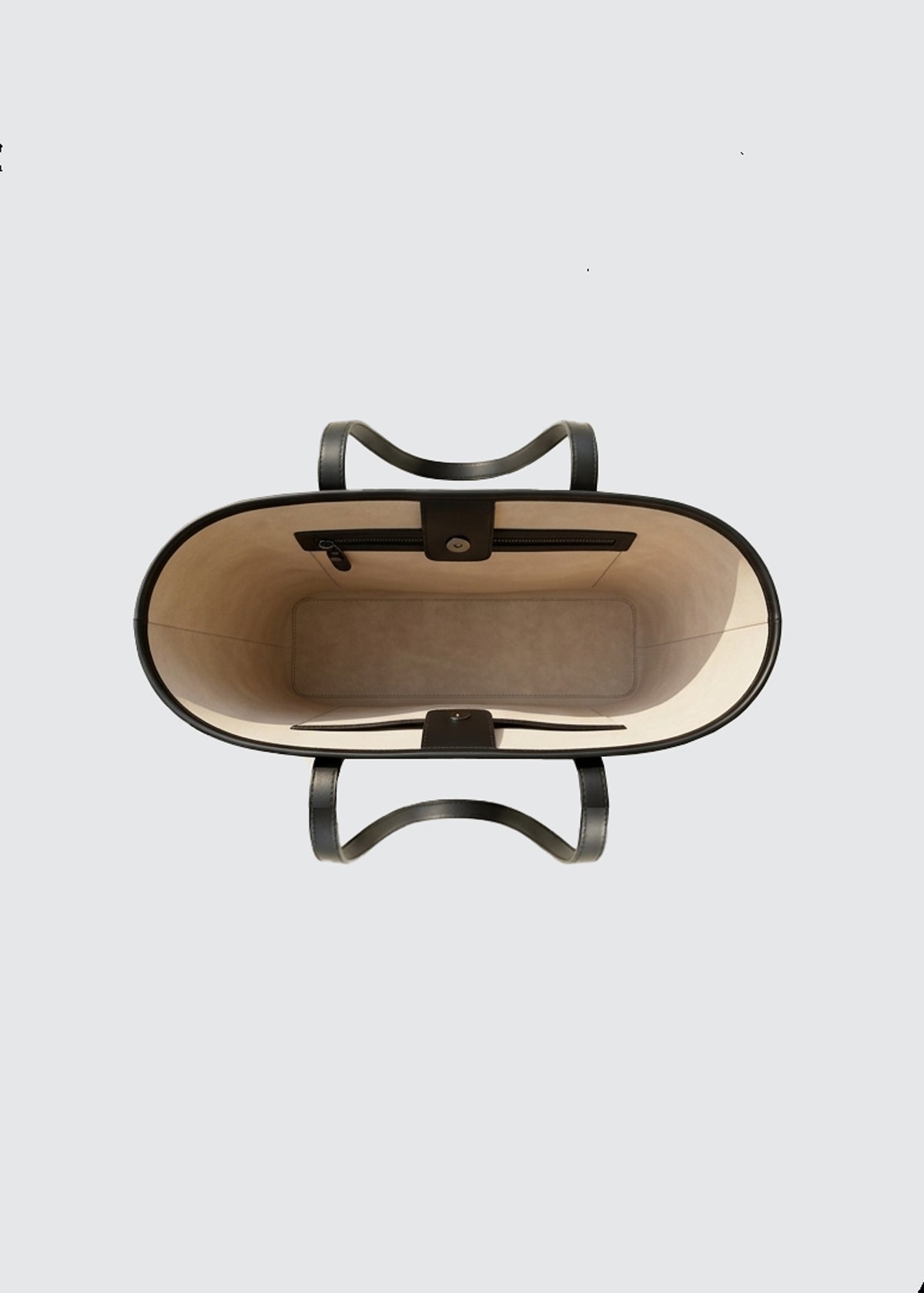 Top-down view of a large tote bag with a beige interior and black leather handles on a light gray background.