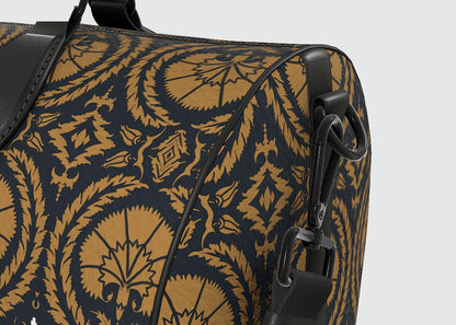 Close-up of a duffel bag featuring a dark navy blue and golden-brown ornate patterned fabric with black leather trim and hardware.