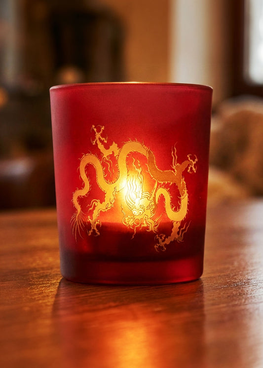 Red candle holder with gold dragon design on a wooden surface.