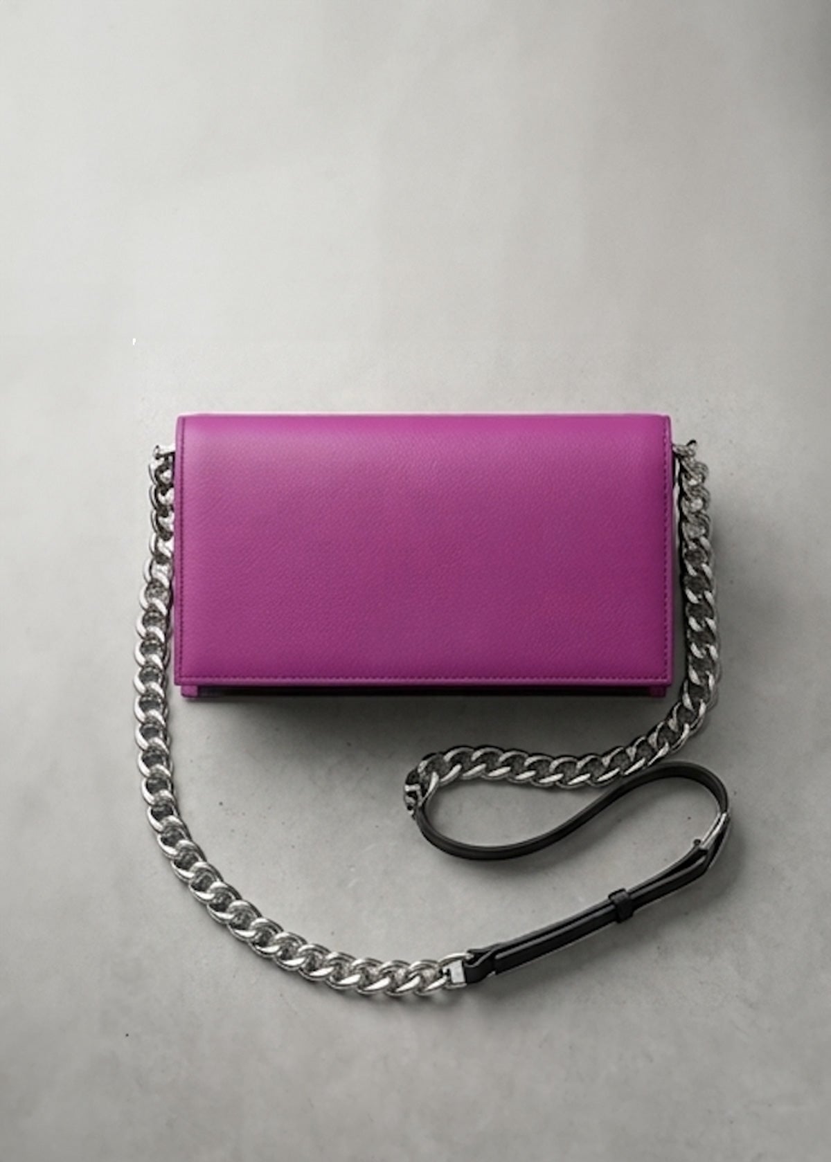 A bright magenta pink leather clutch bag with a silver-tone chain strap and a black leather accent, displayed on a neutral gray background.