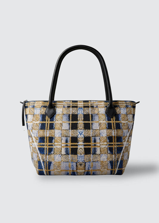 A structured canvas tote bag featuring a complex woven plaid pattern in navy blue, gold, beige, and black, with solid black leather top handles.
