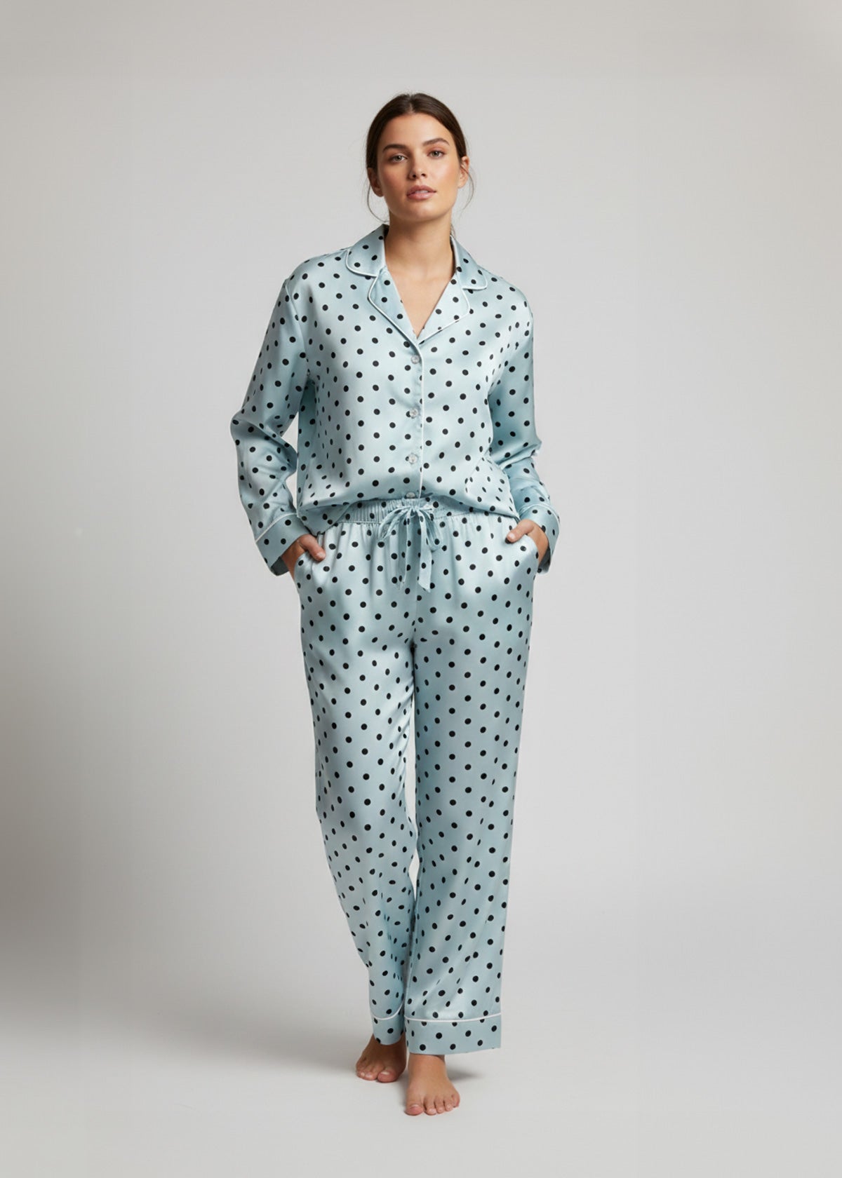 Woman wearing a light blue silkpajama set with black polka dots on a plain background