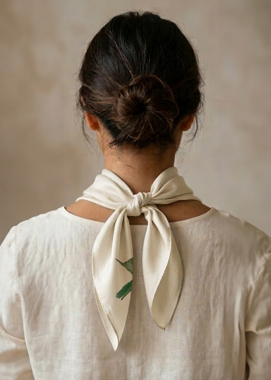 Back view of Woman wearing a cream-colored scarf with a pink and red rose design against a beige background, tied in a cowboy knot.