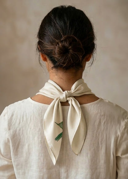 Back view of Woman wearing a cream-colored scarf with a pink and red rose design against a beige background, tied in a cowboy knot.
