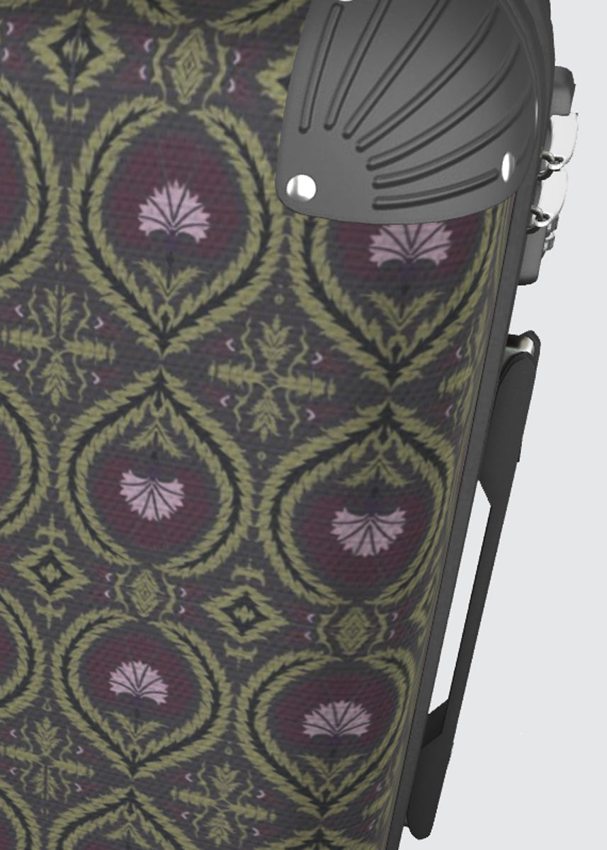 Close-up of a patterned suitcase surface with a repeating ornamental acanthus medallion and wreath design in olive green, burgundy, and lavender, alongside a dark gray moulded plastic corner component.