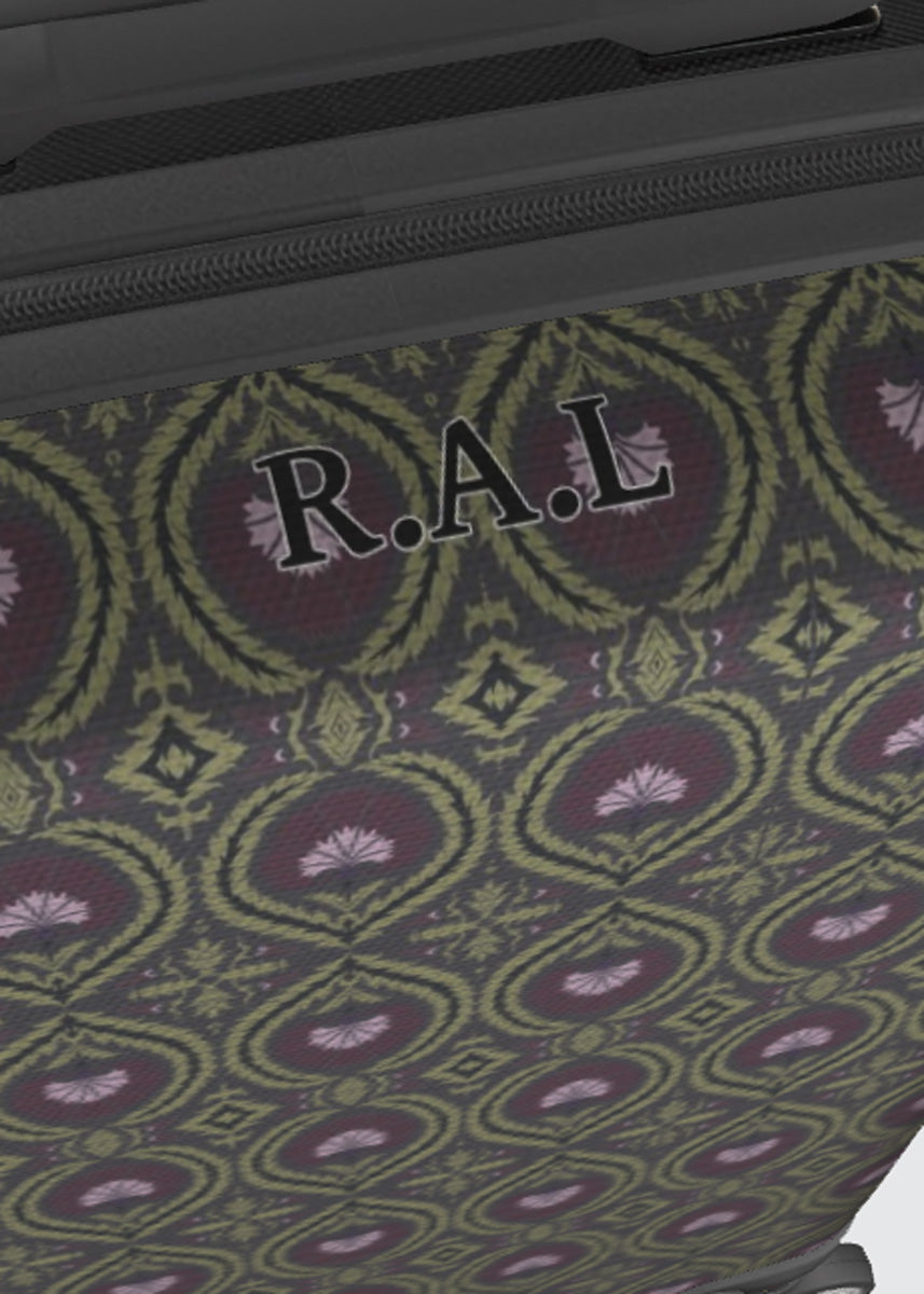 Close-up of a patterned suitcase surface with a repeating ornamental medallion design in olive green, burgundy, and lavender, plus a black zipper and the personalised letters 'R.A.L'.