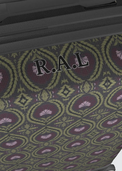 Close-up of a patterned suitcase surface with a repeating ornamental medallion design in olive green, burgundy, and lavender, plus a black zipper and the personalised letters 'R.A.L'.