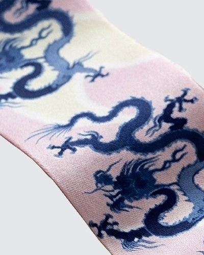 Detail of Skinny hair silk scarf with blue dragons on a pink and cream background.