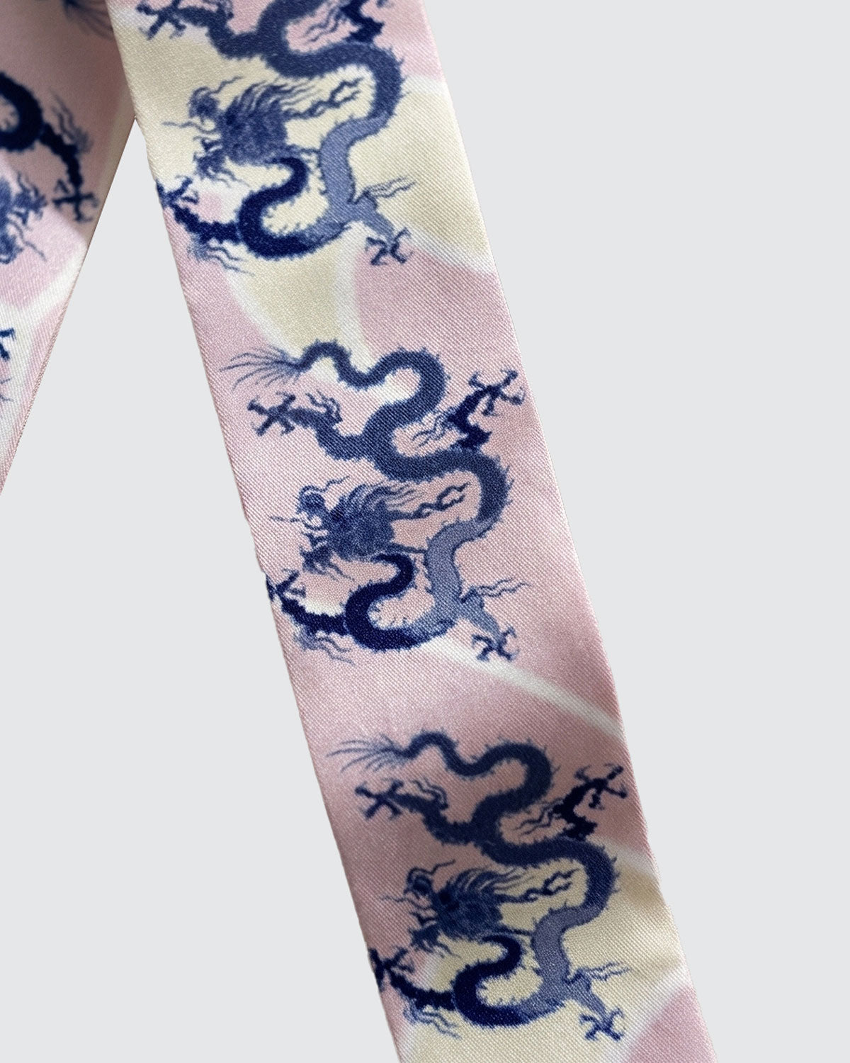 Detail of decorative Skinny hair silk scarf with blue dragons on a pink and cream background.
