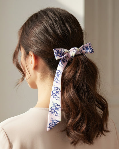 Person with a ponytail tied with a decorative Skinny hair silk scarf with blue dragons on a pink and cream background.