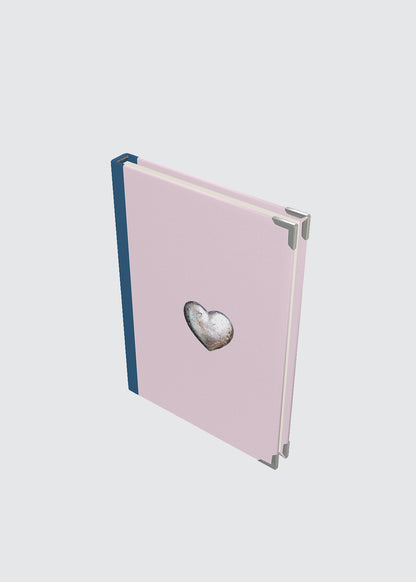 Pink hardback journal notebook with a heart-shaped object.