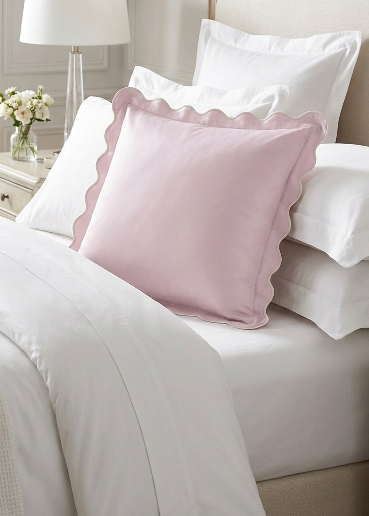Pink square pillow sham with scalloped edges on a bed with white bedding.