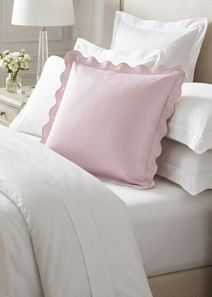 Pink square pillow sham with scalloped edges on a bed with white bedding.