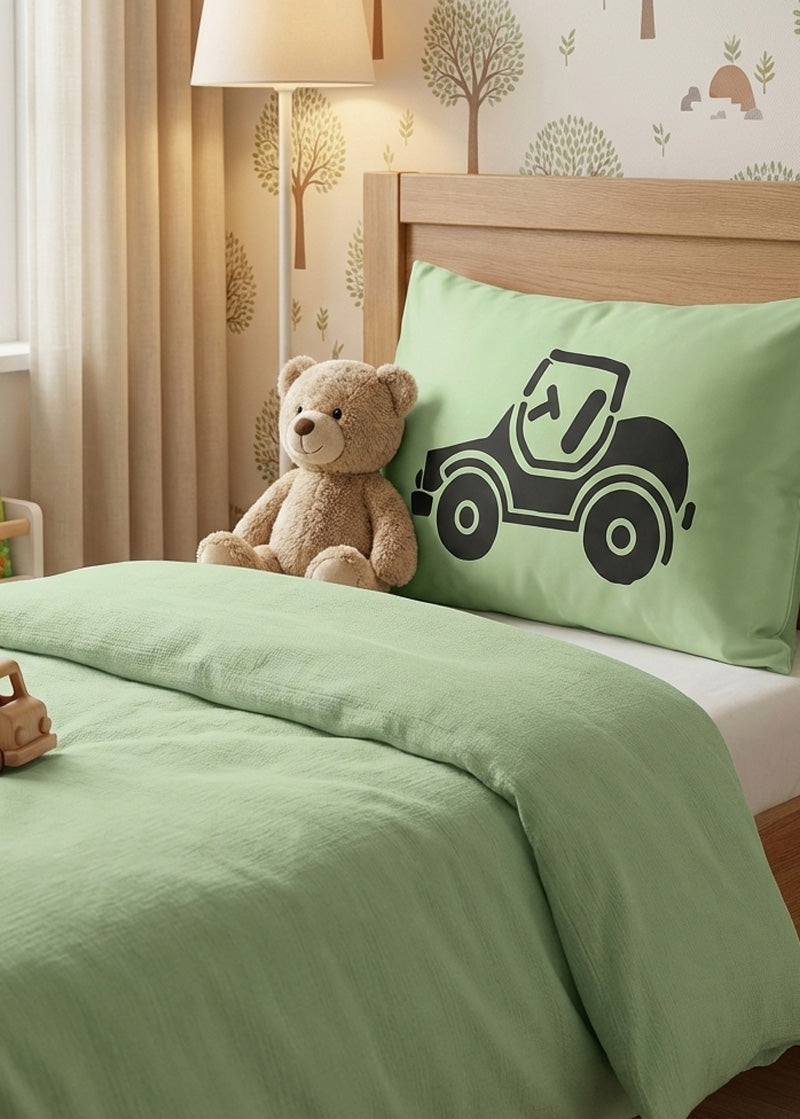 Children's bedroom with green bedding, teddy bear, and green silk pillow with car design.